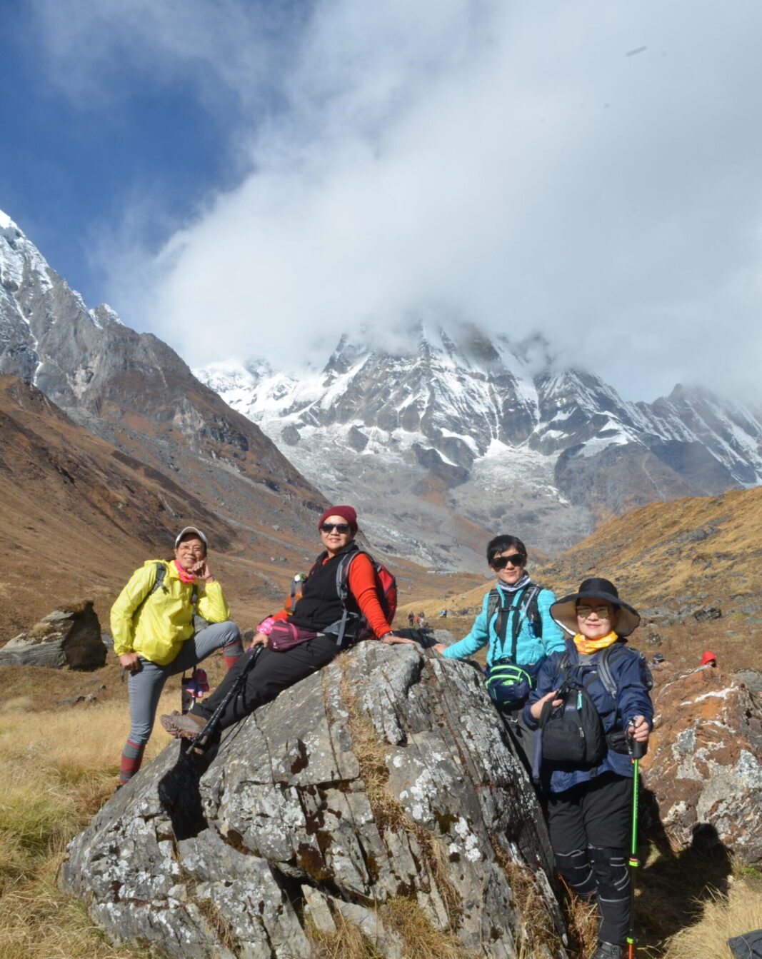 Trekkers taking a group photo at Annapurna Base Camp with panoramic Himalayan mountain views in the background.